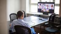 Webinar Mann am Konferenztisch Mann sitzt allein am Konferenztisch; auf der Fensterbank ein Rechner mit Videokonferenz
